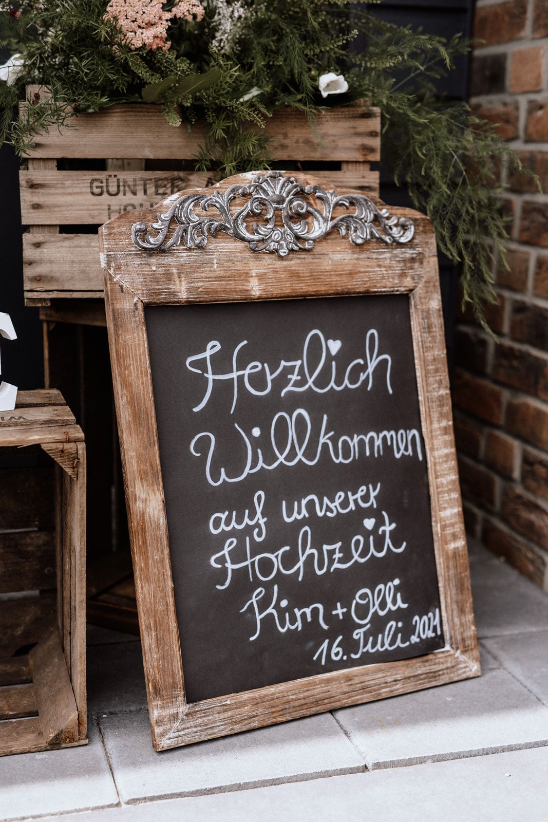 A rustic welcome sign in German with ornate wooden frame announcing a wedding date.