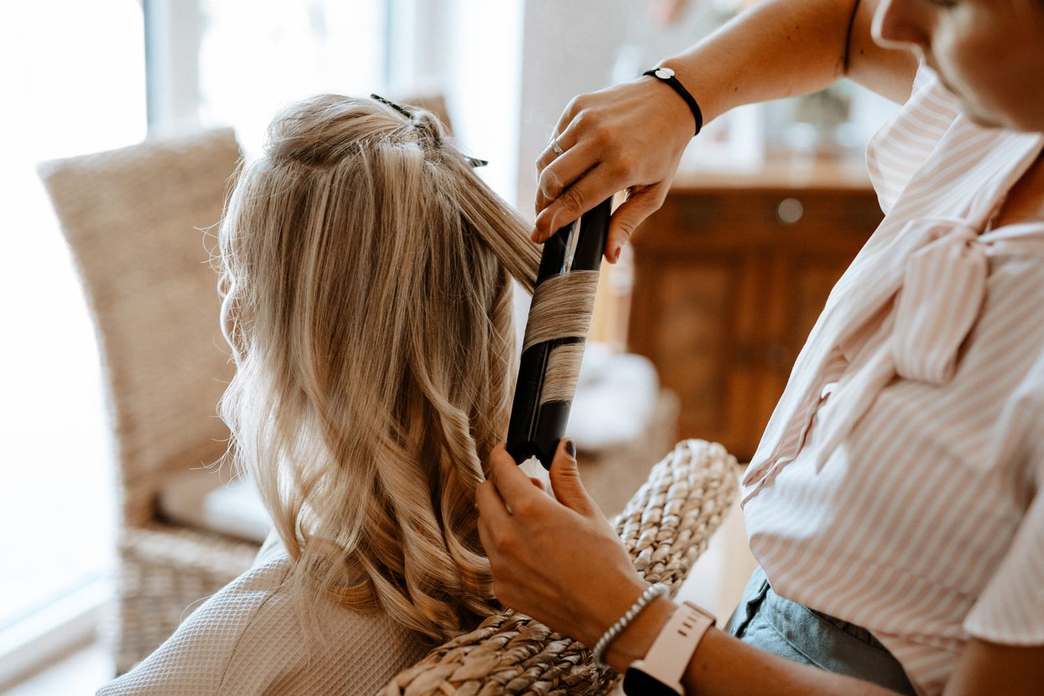 Hair stylist creating elegant curls and styling for a wedding preparation.