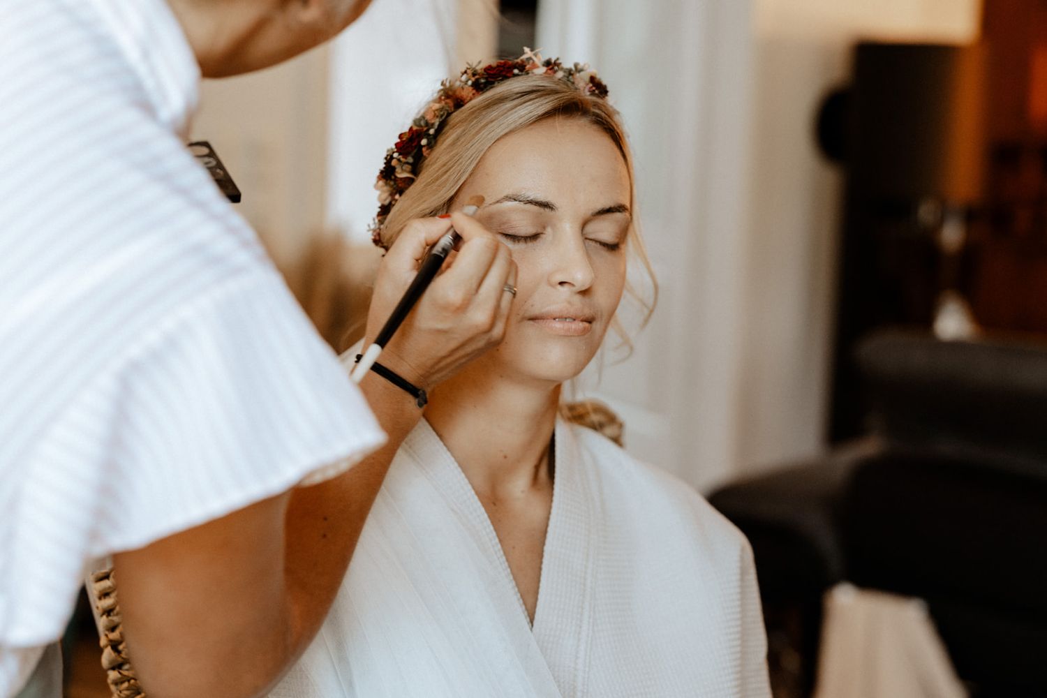 A bridal preparation moment showing makeup application in a bright room.
