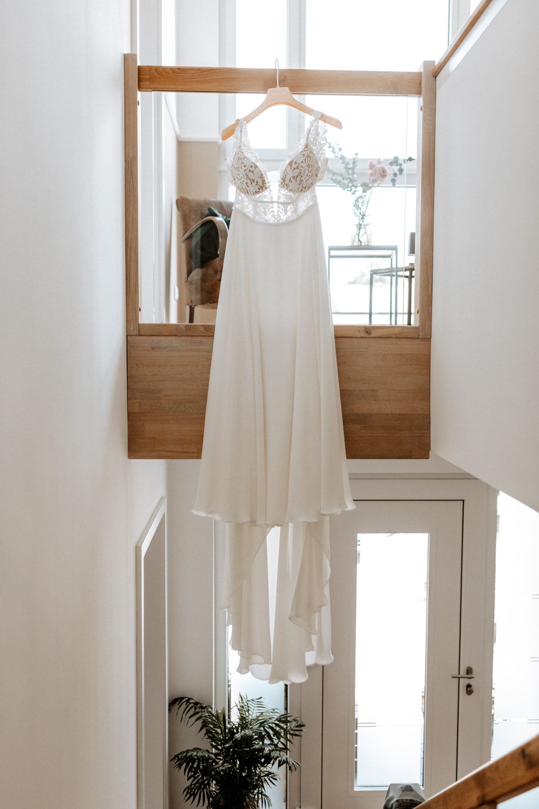 An elegant white wedding dress with lace details hanging in a bright, modern interior.
