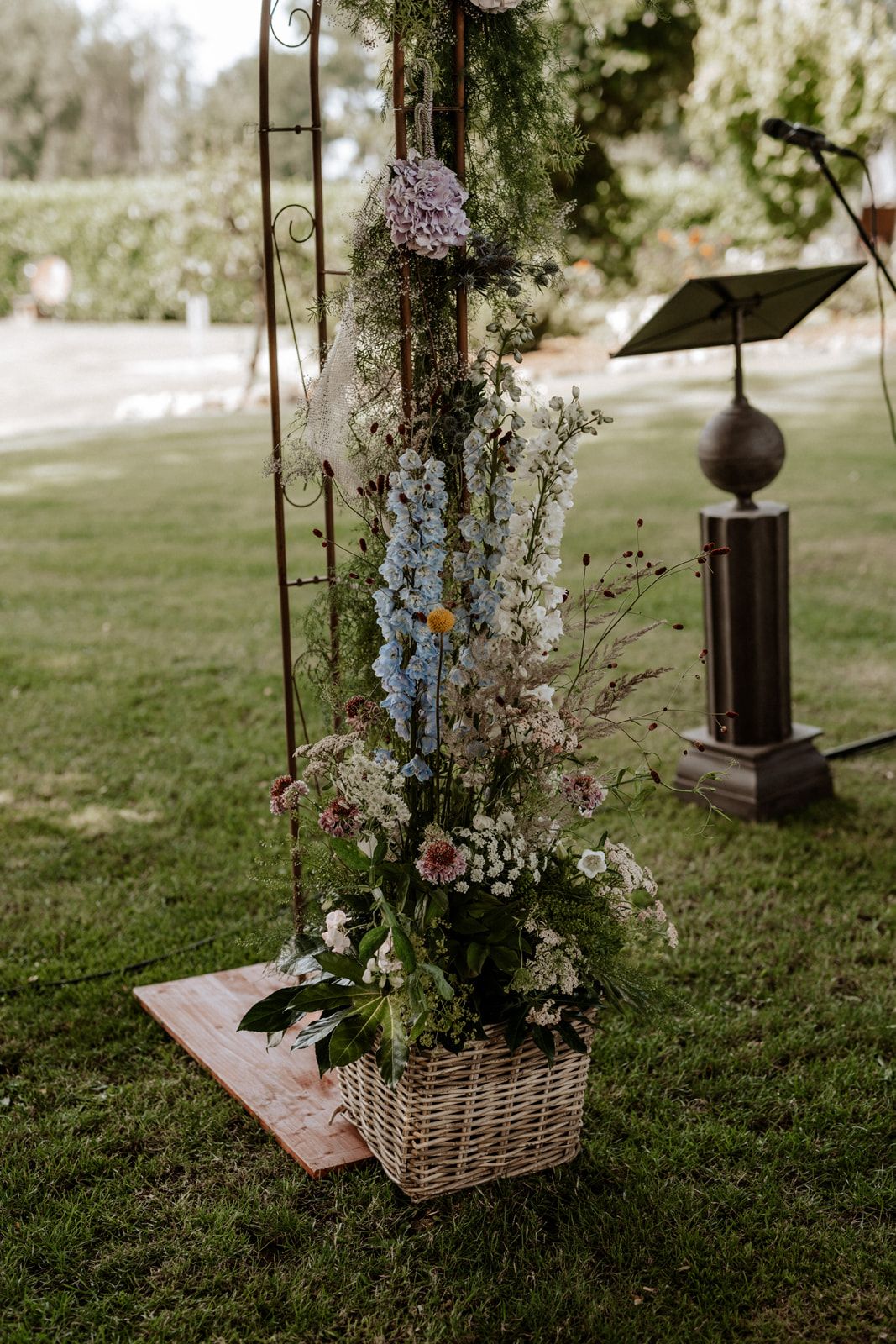 A tall rustic flower arrangement in a wicker basket featuring wildflowers and garden blooms.