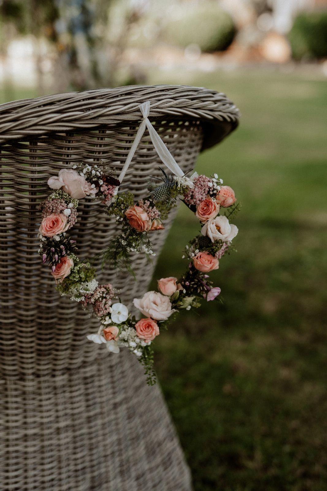 A delicate floral heart wreath with pink roses hanging on a wicker basket.