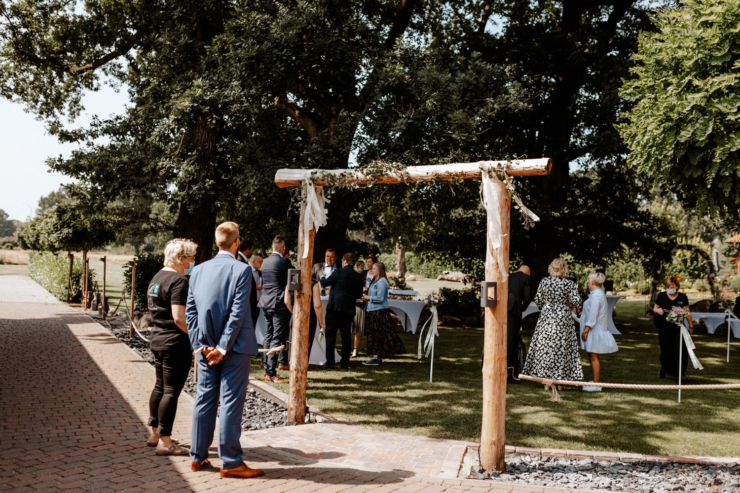 Rustic wooden arch entrance to outdoor wedding ceremony with guests gathering.