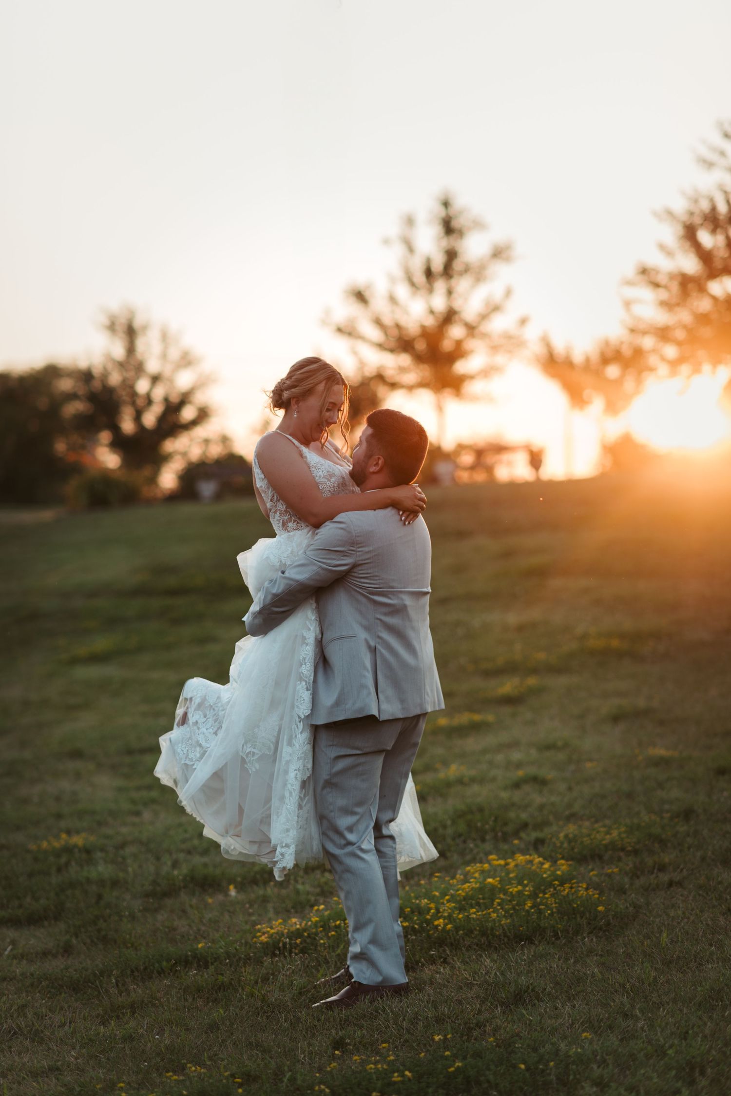 Romantic couple embracing at sunset in a field with bride's dress flowing in the breeze.