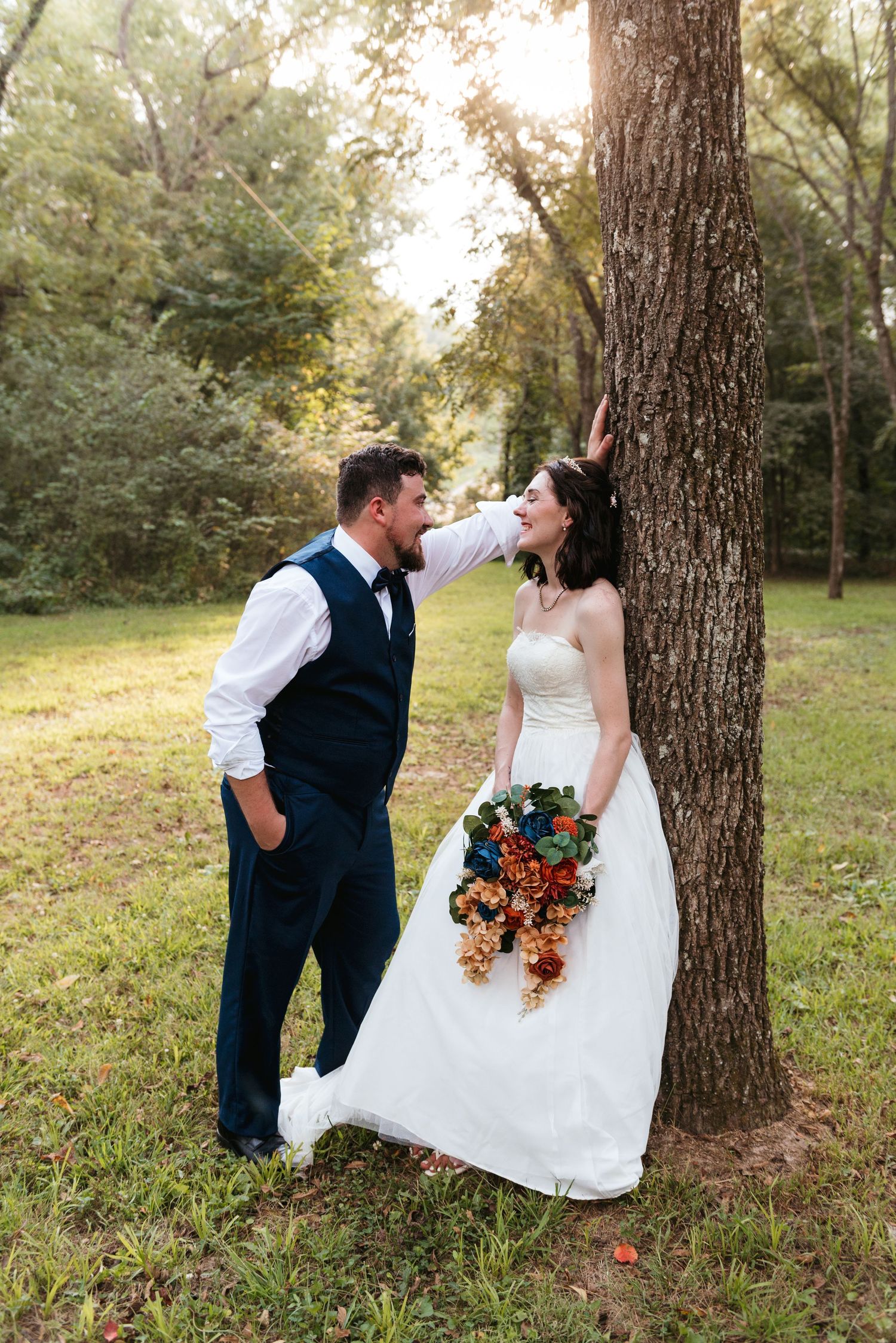 A romantic woodland wedding portrait with a couple posed against a large tree trunk.