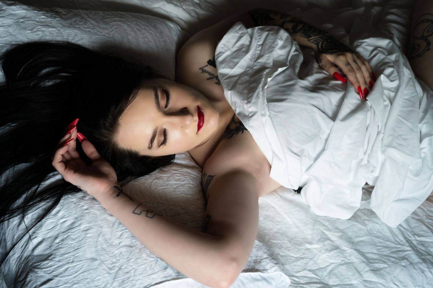 Woman in white dress lying peacefully on bed with dark hair spread out.