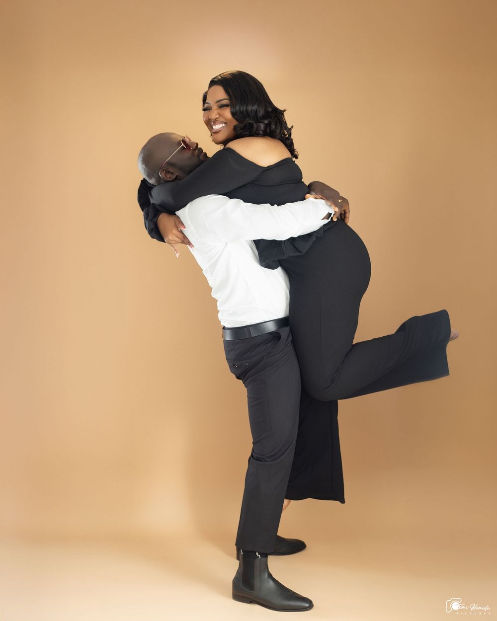 Two dancers in black and white outfits perform an intimate partner dance sequence against a beige backdrop.