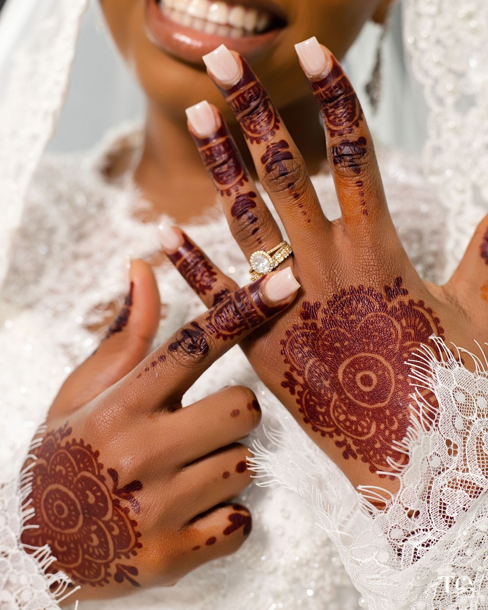 Bride displays intricate henna mehndi designs on both hands, wearing a diamond engagement ring and pink nails.