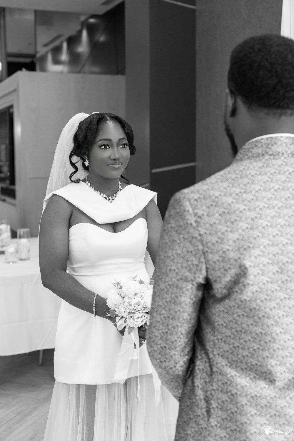 A person in a white dress stands in an elegant indoor setting during what appears to be a wedding celebration.