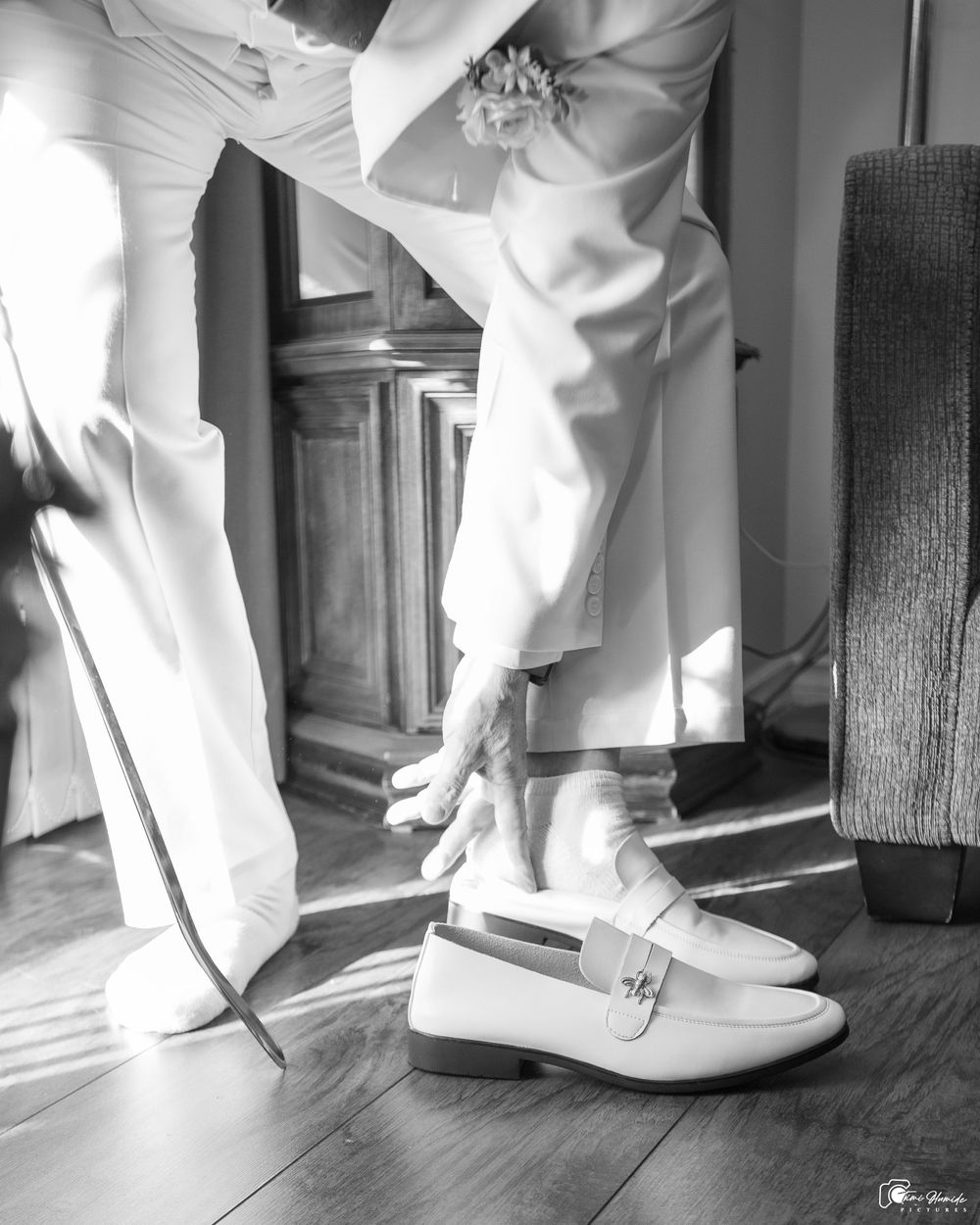 Black and white photo showing legs in white pants and light-colored loafers standing on a hardwood floor in sunlight.