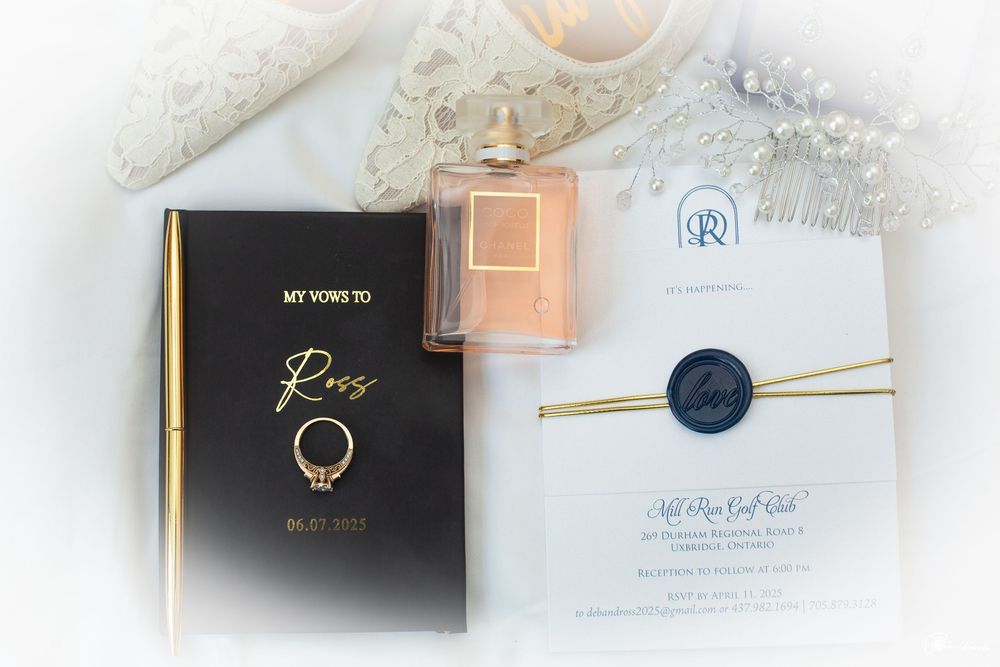 Elegant wedding invitation setup with perfume bottle, black and gold book, and decorative navy blue wax seal details.