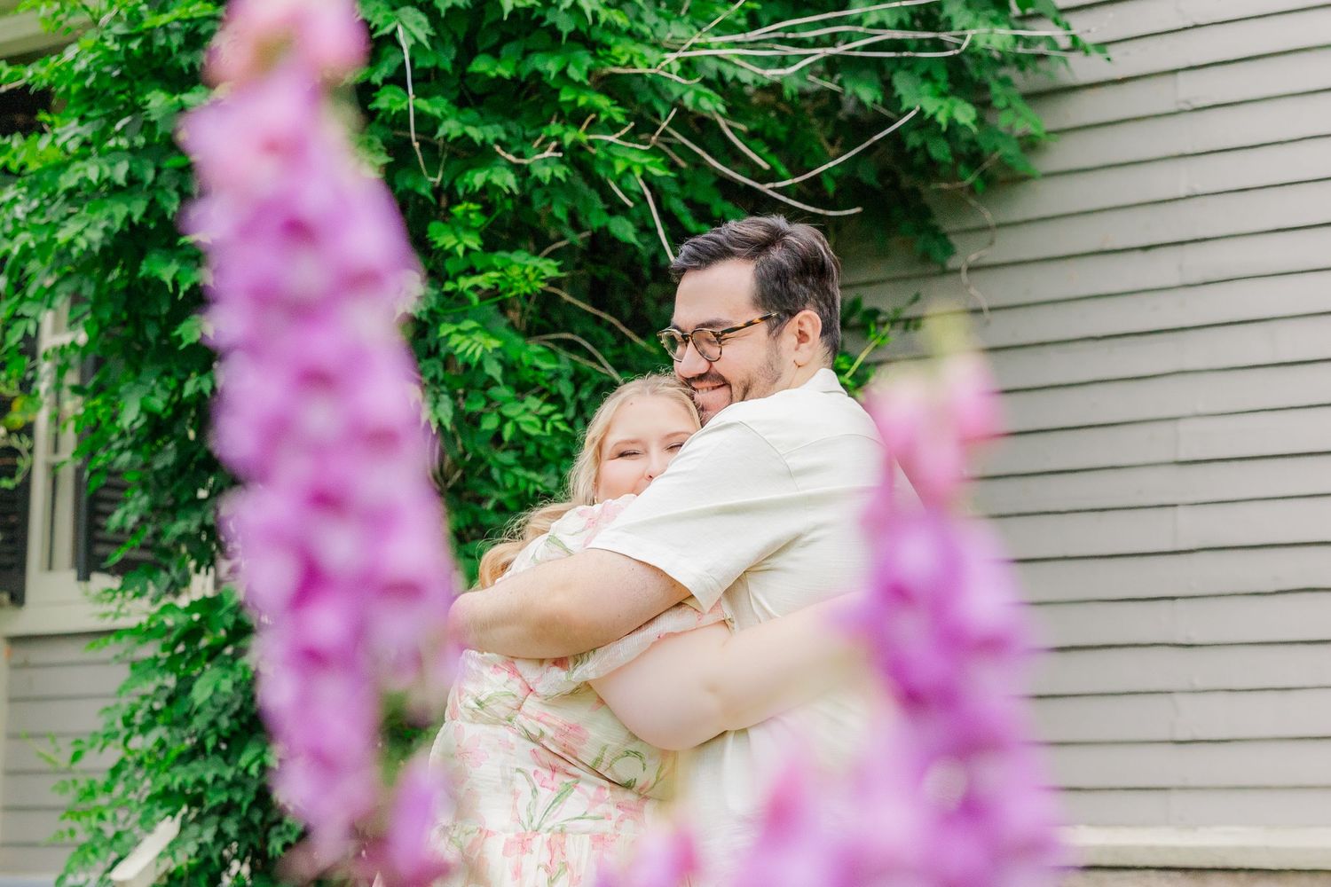 A tender embrace captured through blooming pink foxglove flowers against a house with green climbing vines.