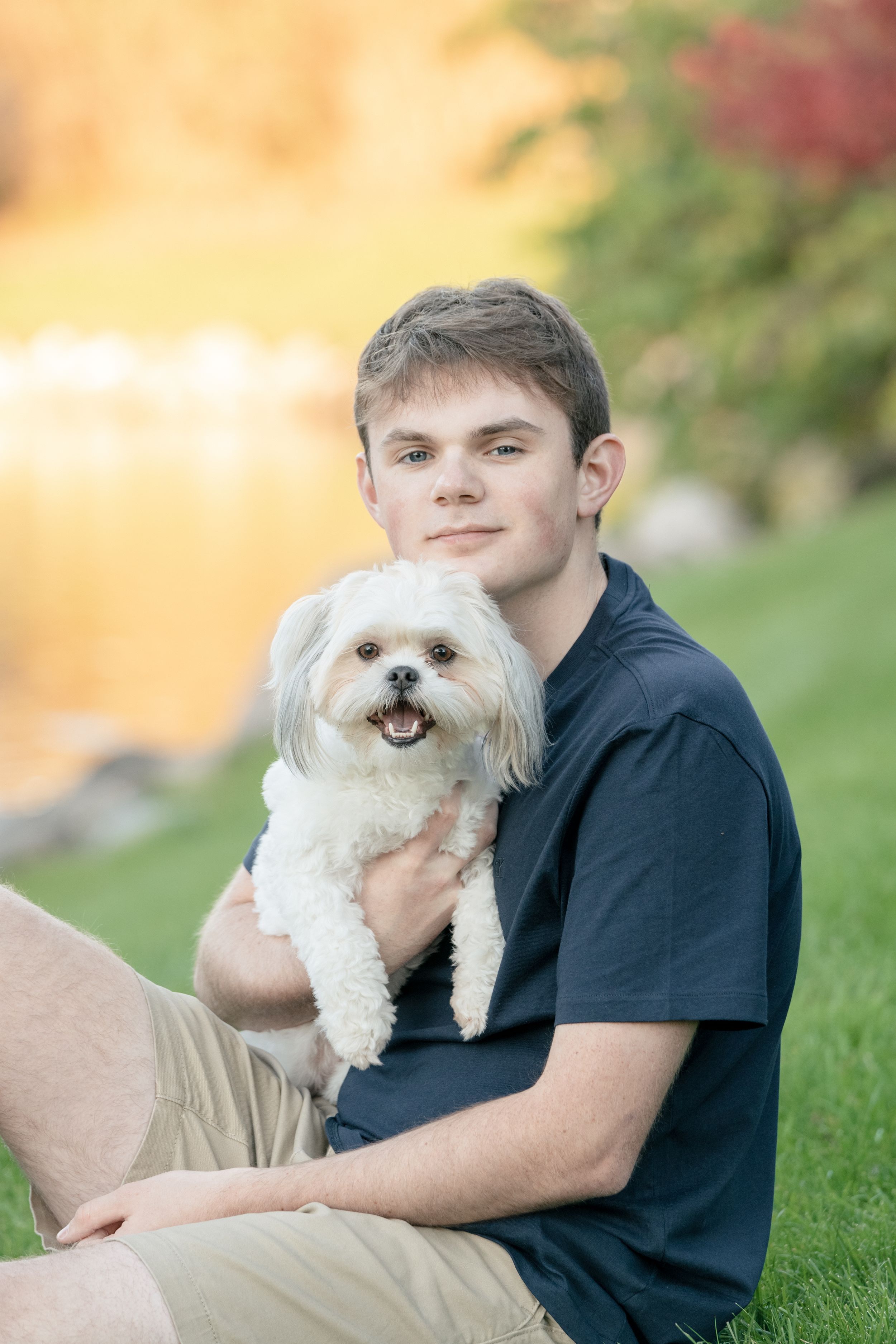 Small white fluffy dog smiling and being held lovingly on green grass in a sunny outdoor setting.