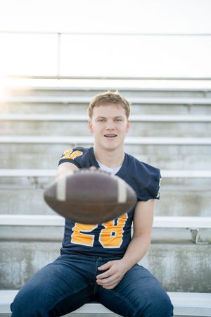 Individual in navy shirt sits on bleachers holding football while photographed from different angles.