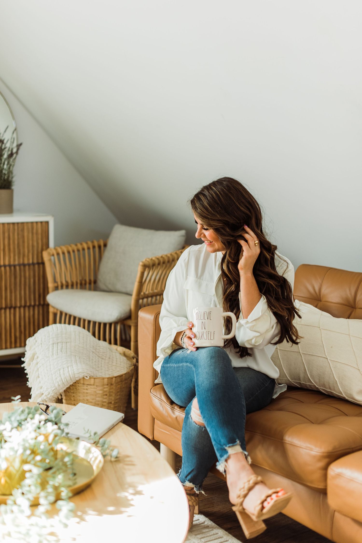 Person sitting on brown leather couch using a white pillow to hide and curl up in a cozy attic room.