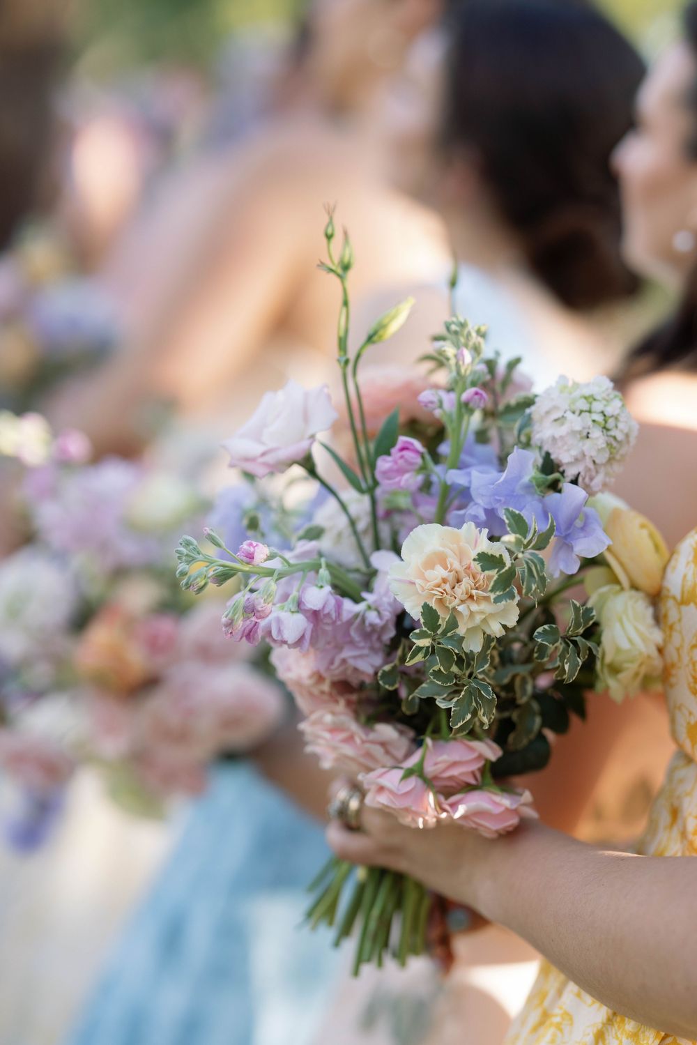 Delicate pastel wedding bouquet with purple, blue and cream flowers held against a light blue bridesmaid dress.