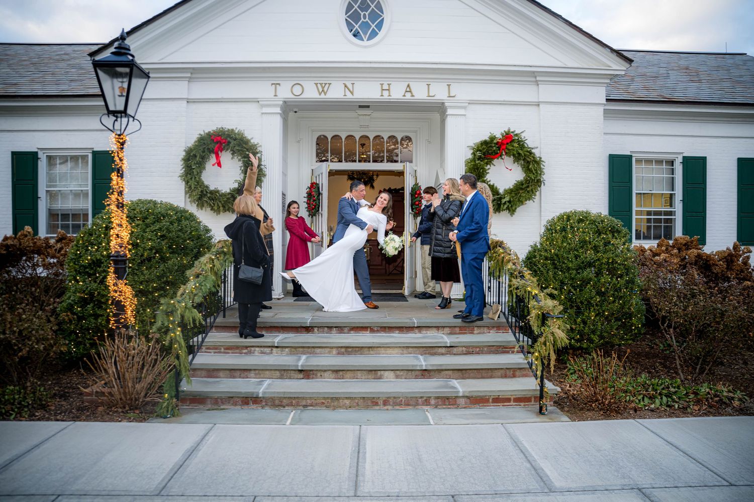 A festive town hall entrance decorated with holiday wreaths and lights hosts a winter wedding ceremony on the front steps.