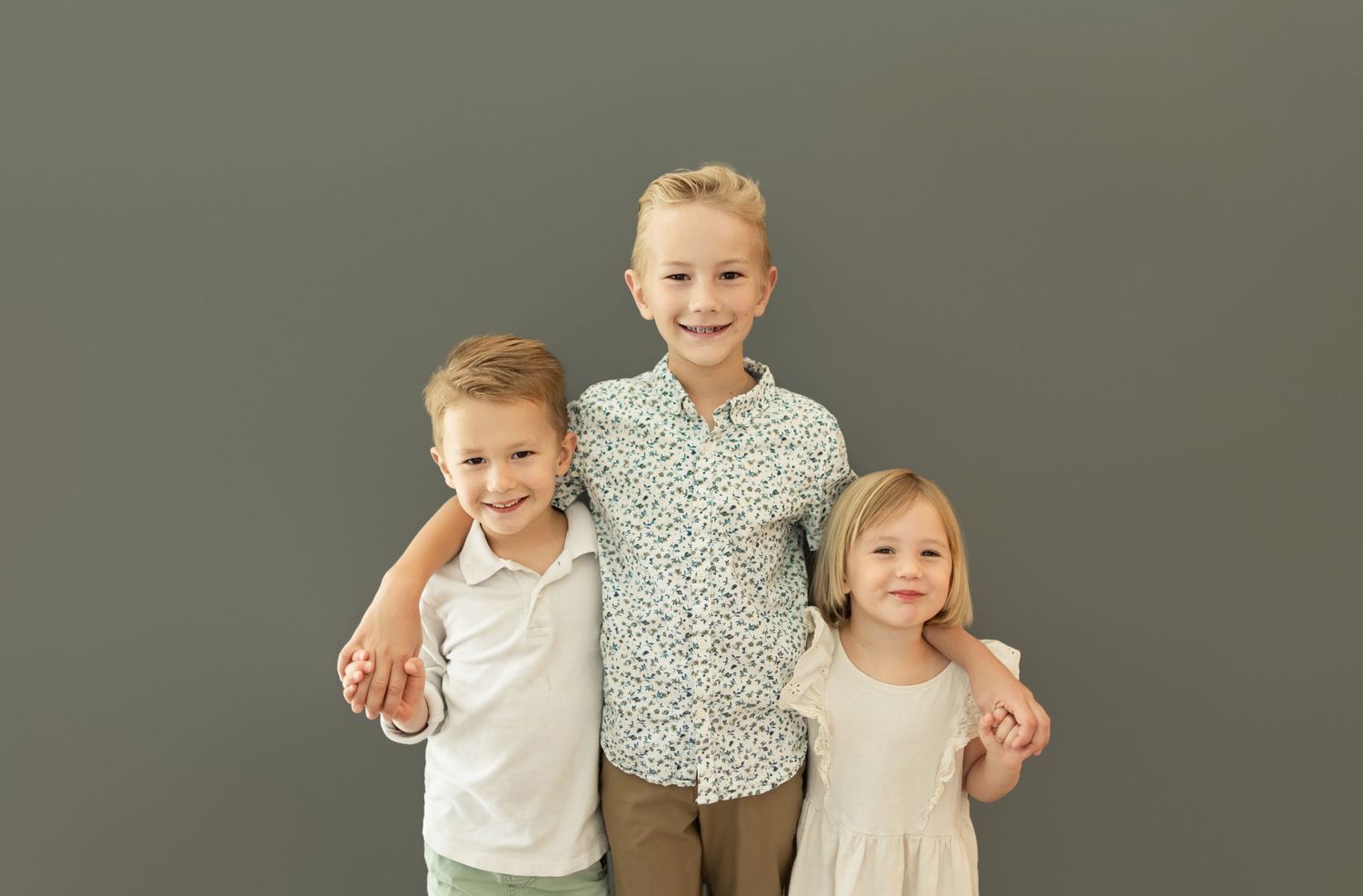 Studio family portrait session against simple gray backdrop with casual styling.