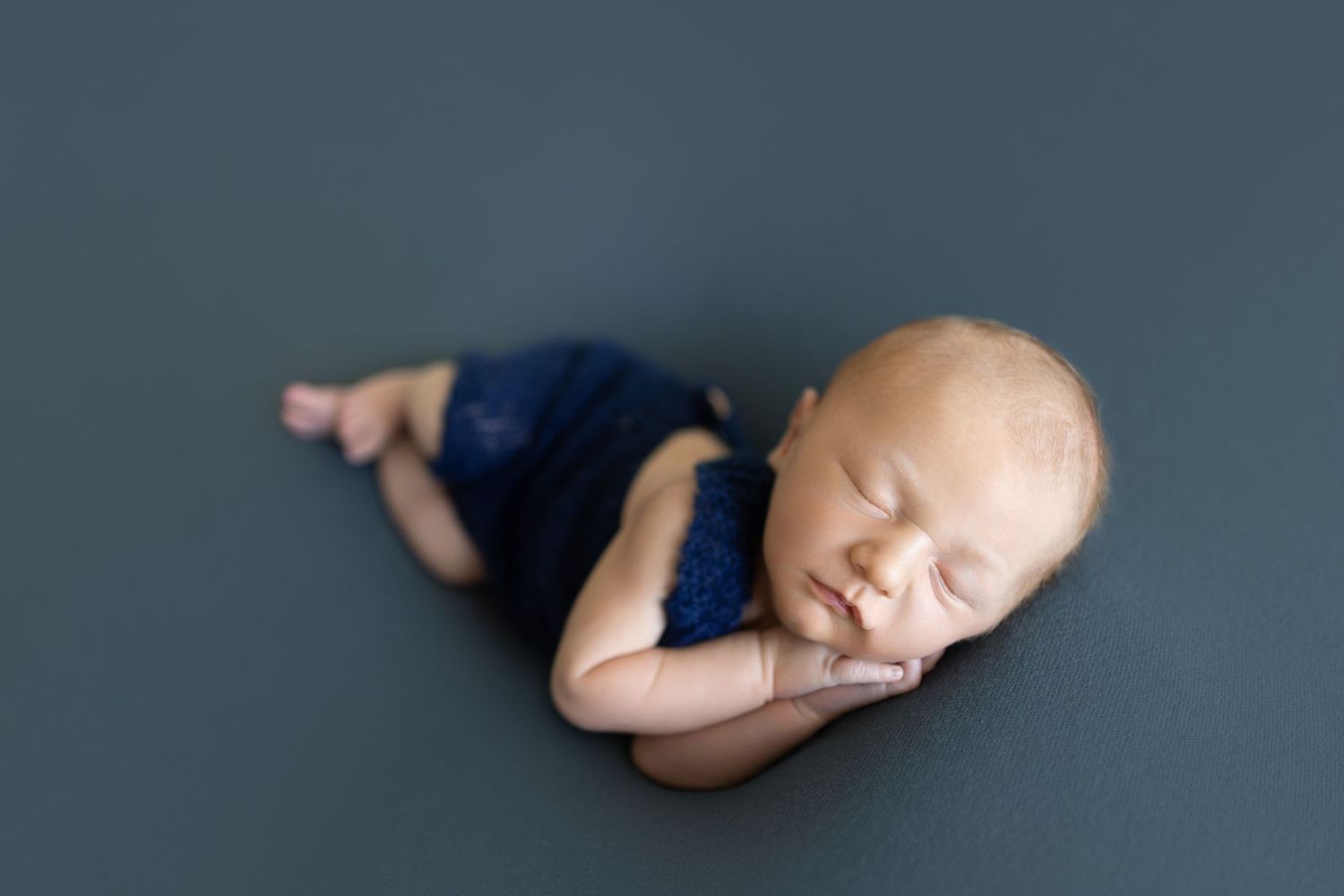 Sleeping newborn baby wearing navy blue outfit lying on dark grey background. Photos by Tampa Photographer DigitalMyst Photography