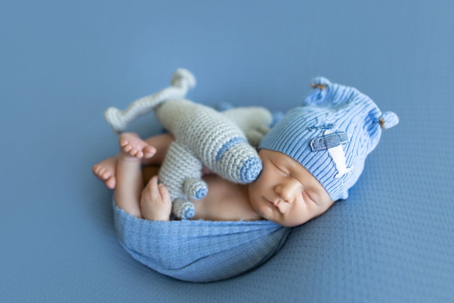 Sleeping newborn in blue and white striped outfit resting on curved cushion. Photos by Tampa Photographer DigitalMyst Photography