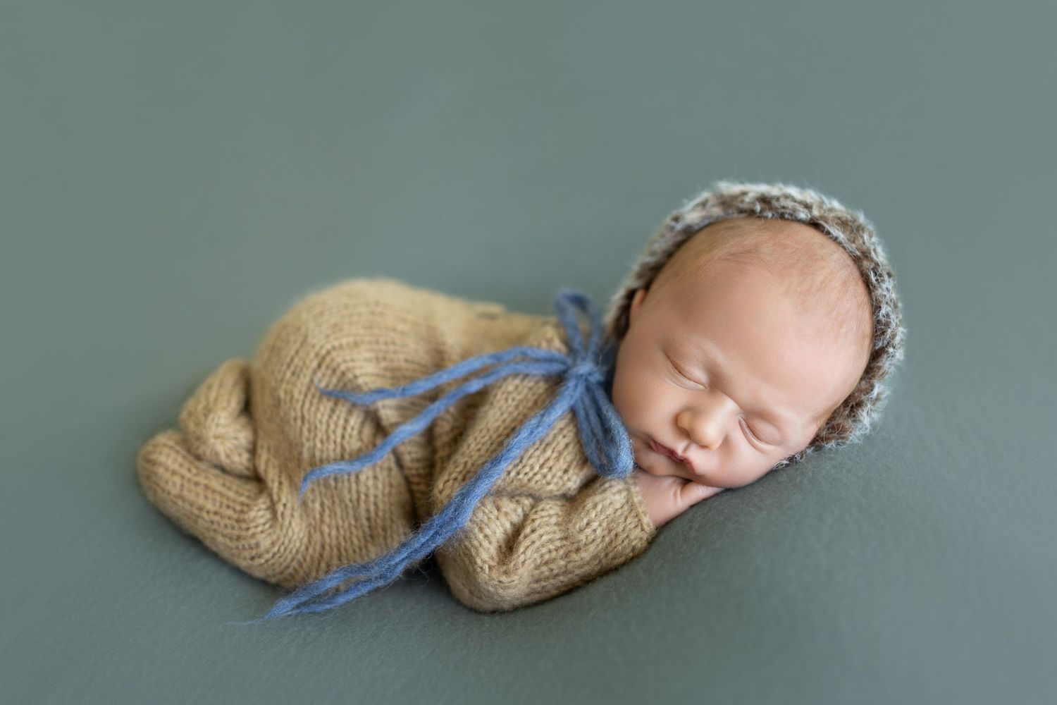 Peaceful sleeping newborn in tan knit wrap with blue ribbon. Photos by Tampa Photographer DigitalMyst Photography