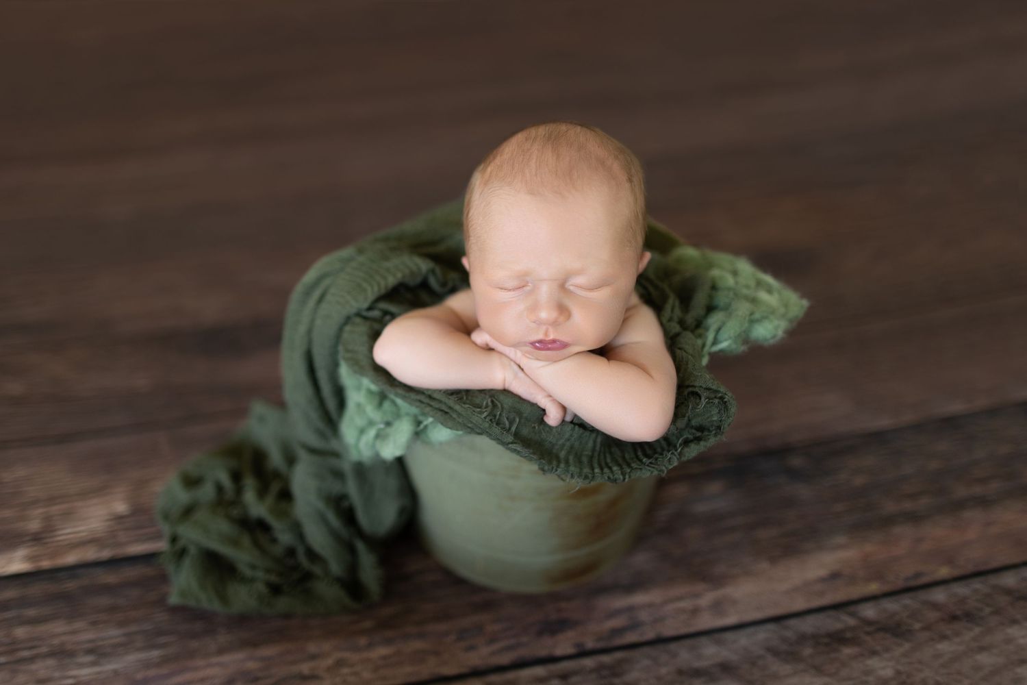 Sleeping newborn nestled in green bowl on wooden surface. Photos by Tampa Photographer DigitalMyst Photography