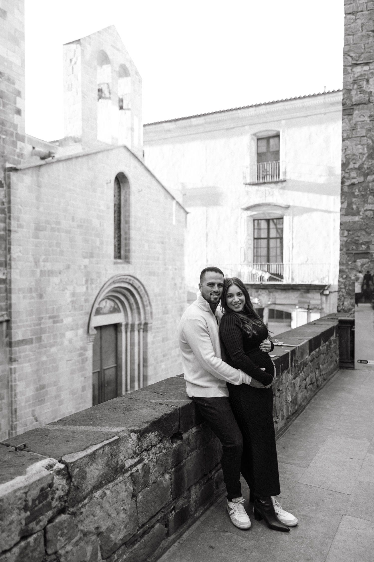 Couple poses along stone balustrade with Gothic cathedral architecture in background.