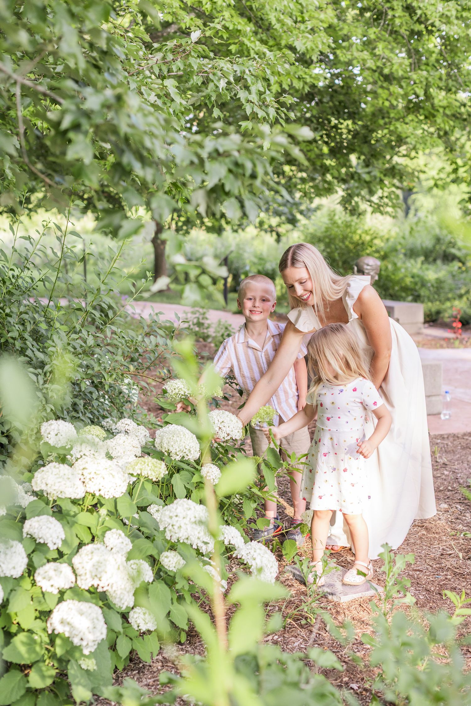 Two people sit on a white blanket under blooming trees for an outdoor photo session at sunset.