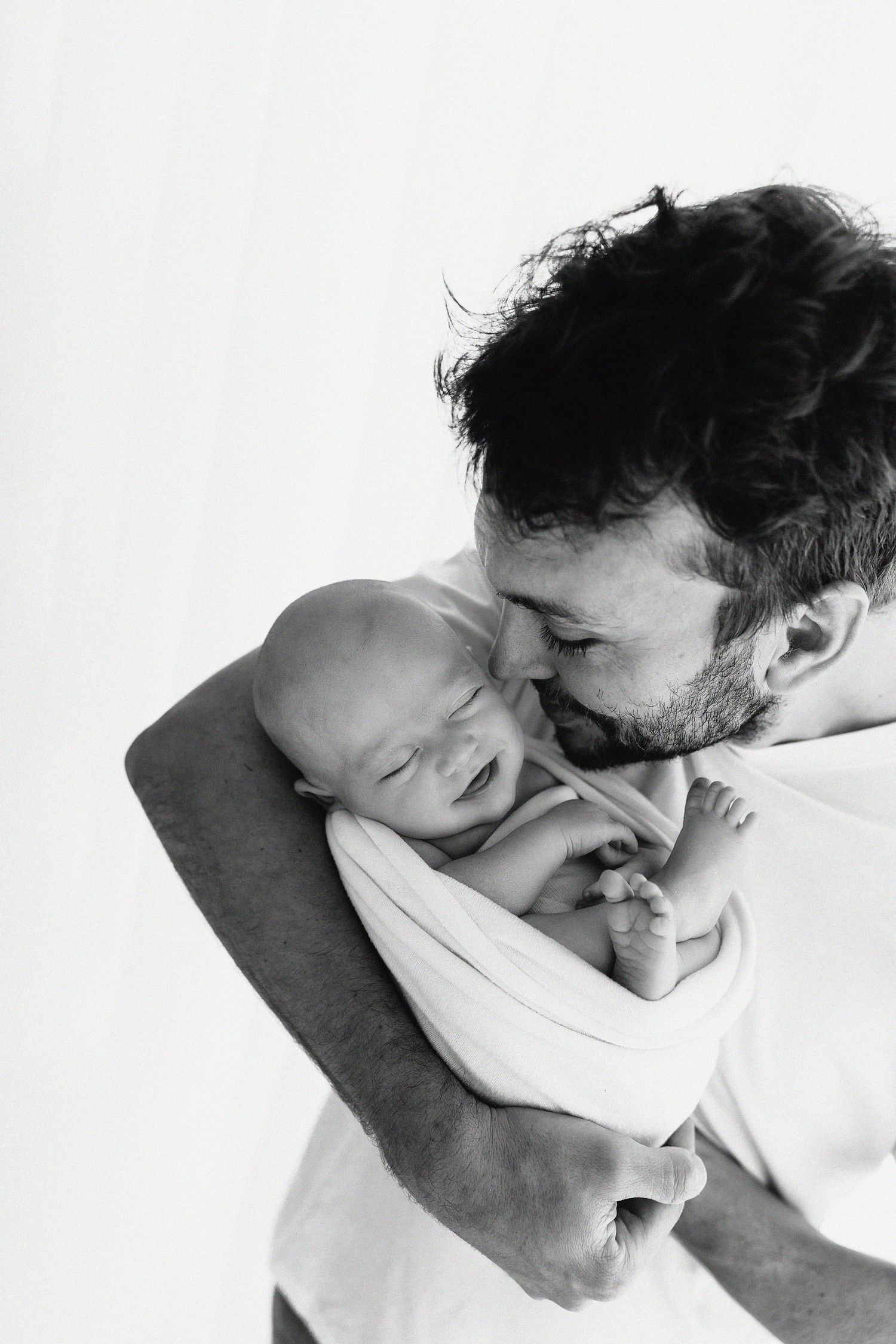 Three sequential monochrome photos showing tender emotional interaction between a father and baby in white light.