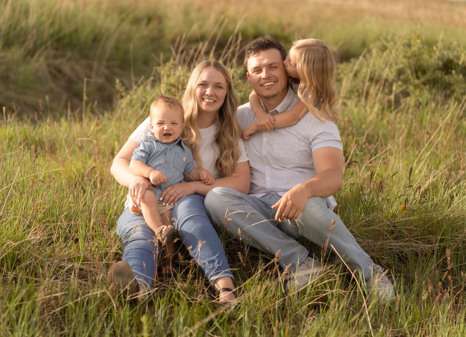 Family of four sitting and posing for a family session on a sunny mountainside in Logan UT with their local photographer.