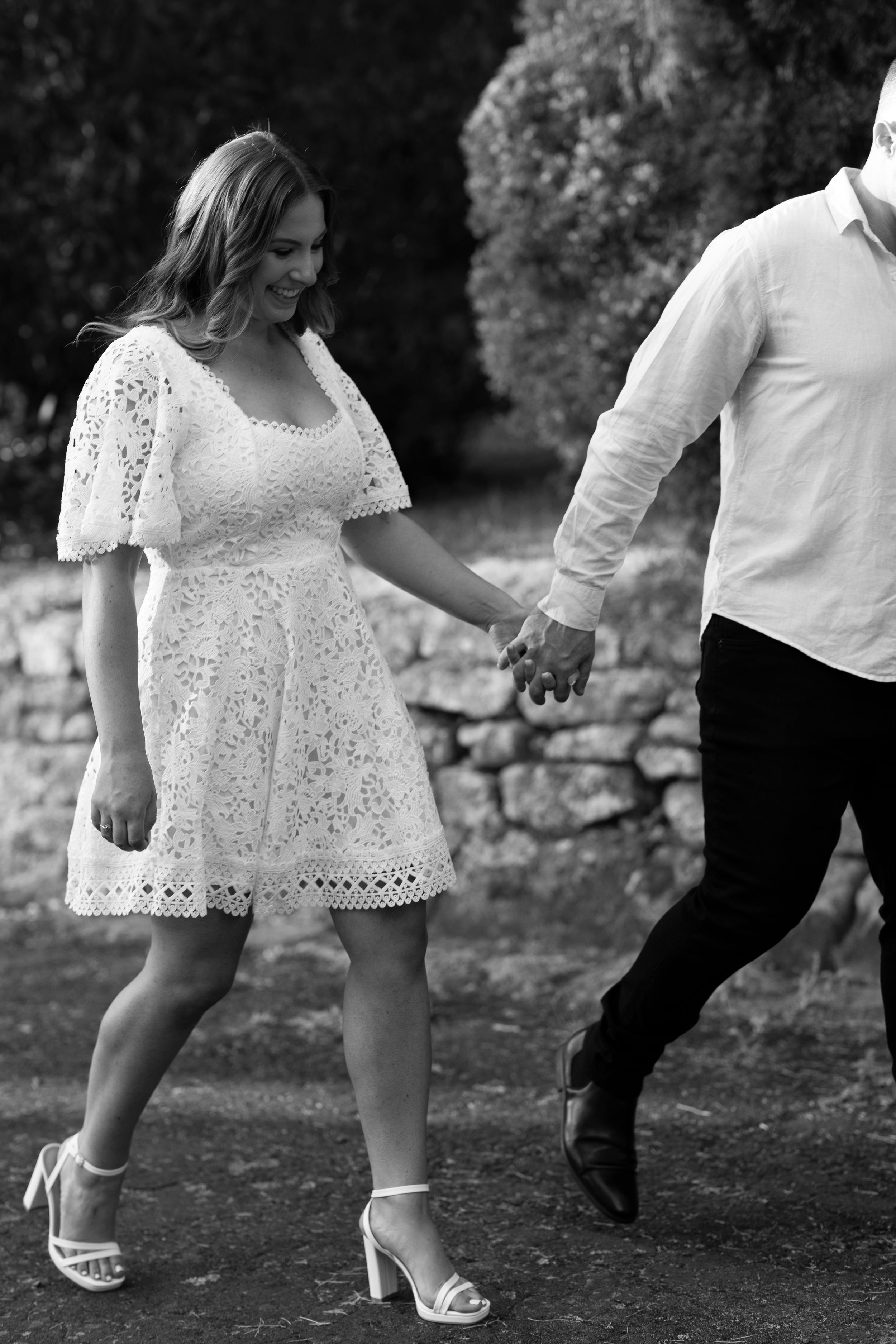 Couple holding hands while walking outdoors in formal attire for engagement photos.