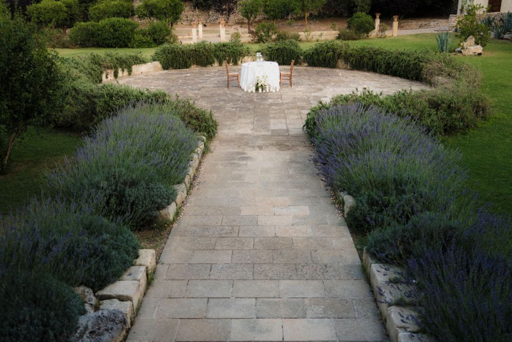 Stone path lined with lavender leads to white chairs arranged in a garden patio setting.