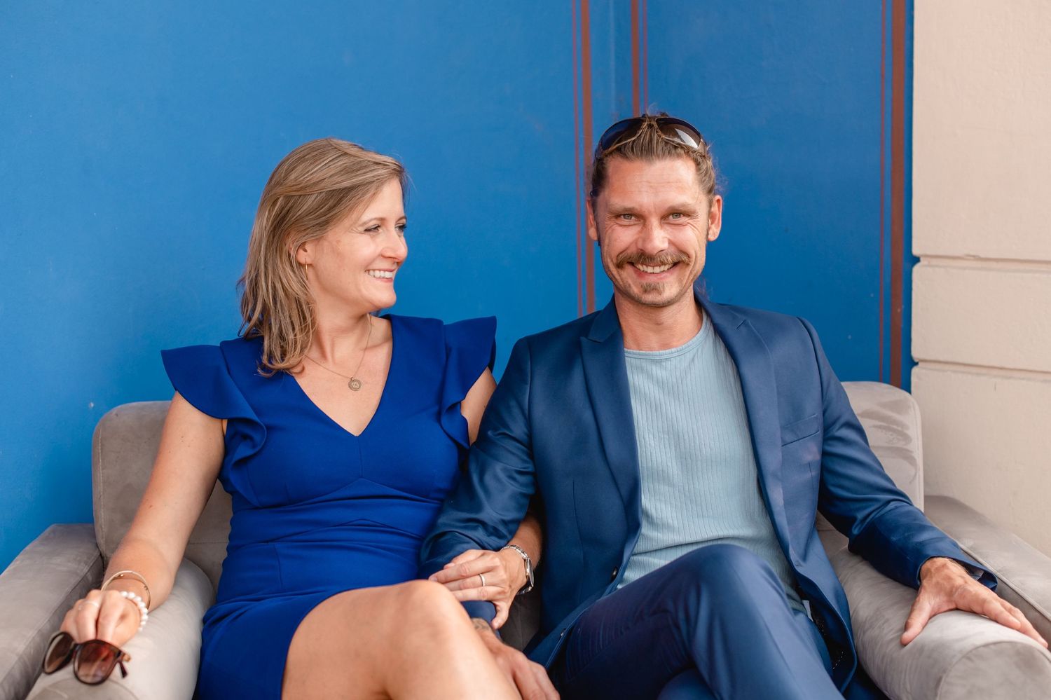 Wedding planner couple sitting together on a grey couch against a bright blue wall. Weddings by MyCastleWedding | Dresden.