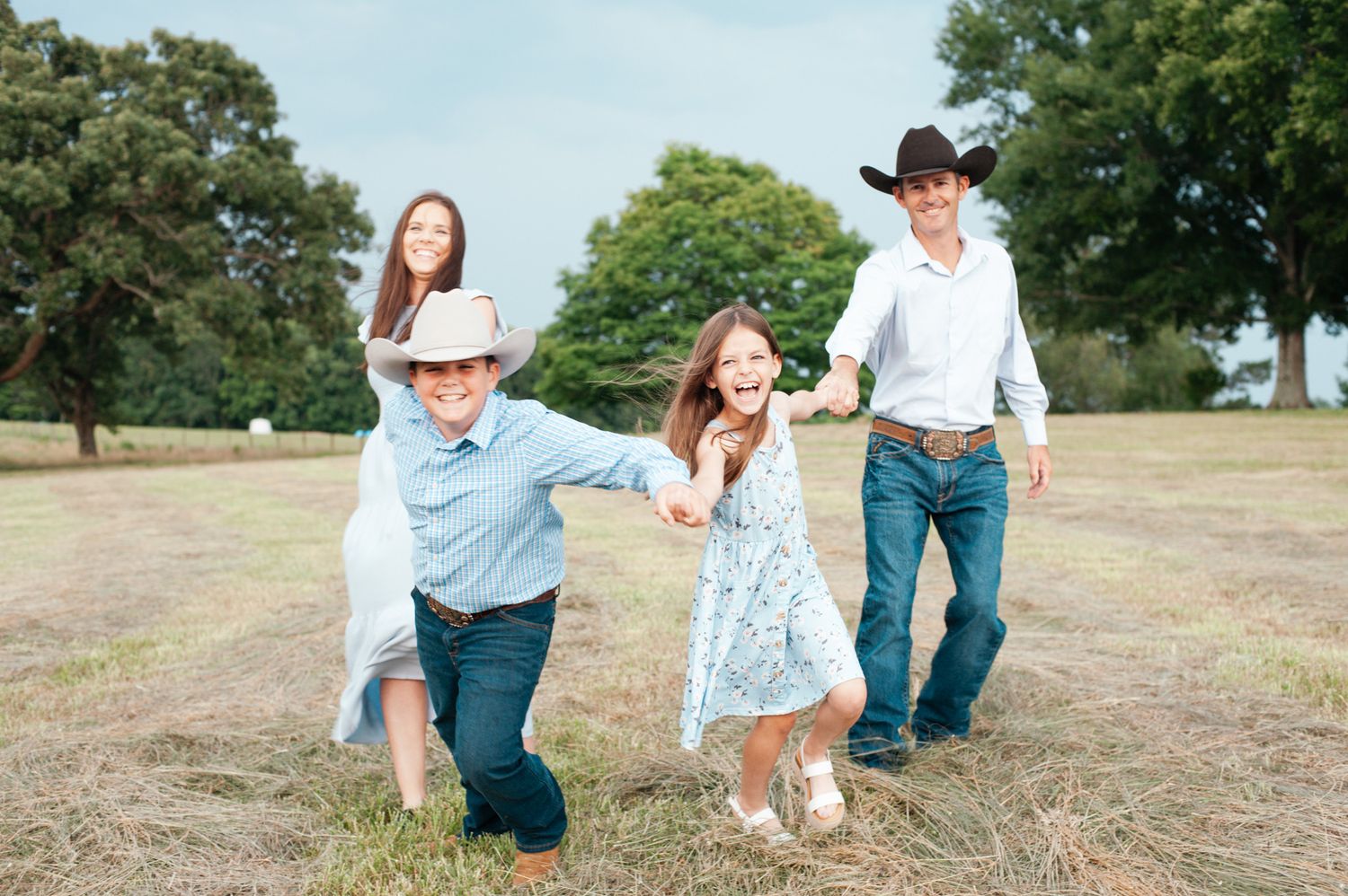 Family in casual attire playfully interacts on a grassy hill during a summer outdoor photoshoot session.
