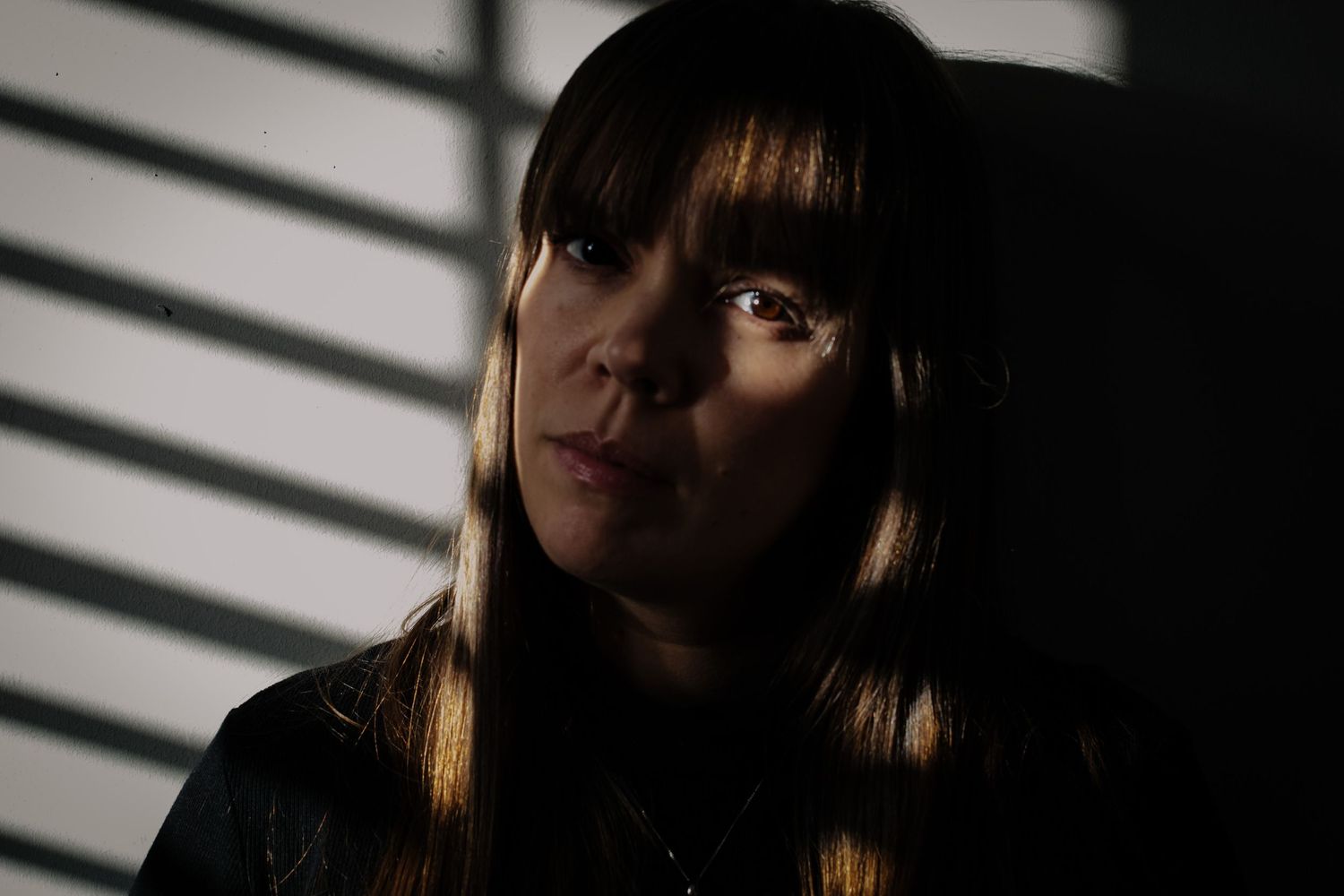 A monochromatic portrait shows someone in dramatic lighting with horizontal blinds casting striped shadows.