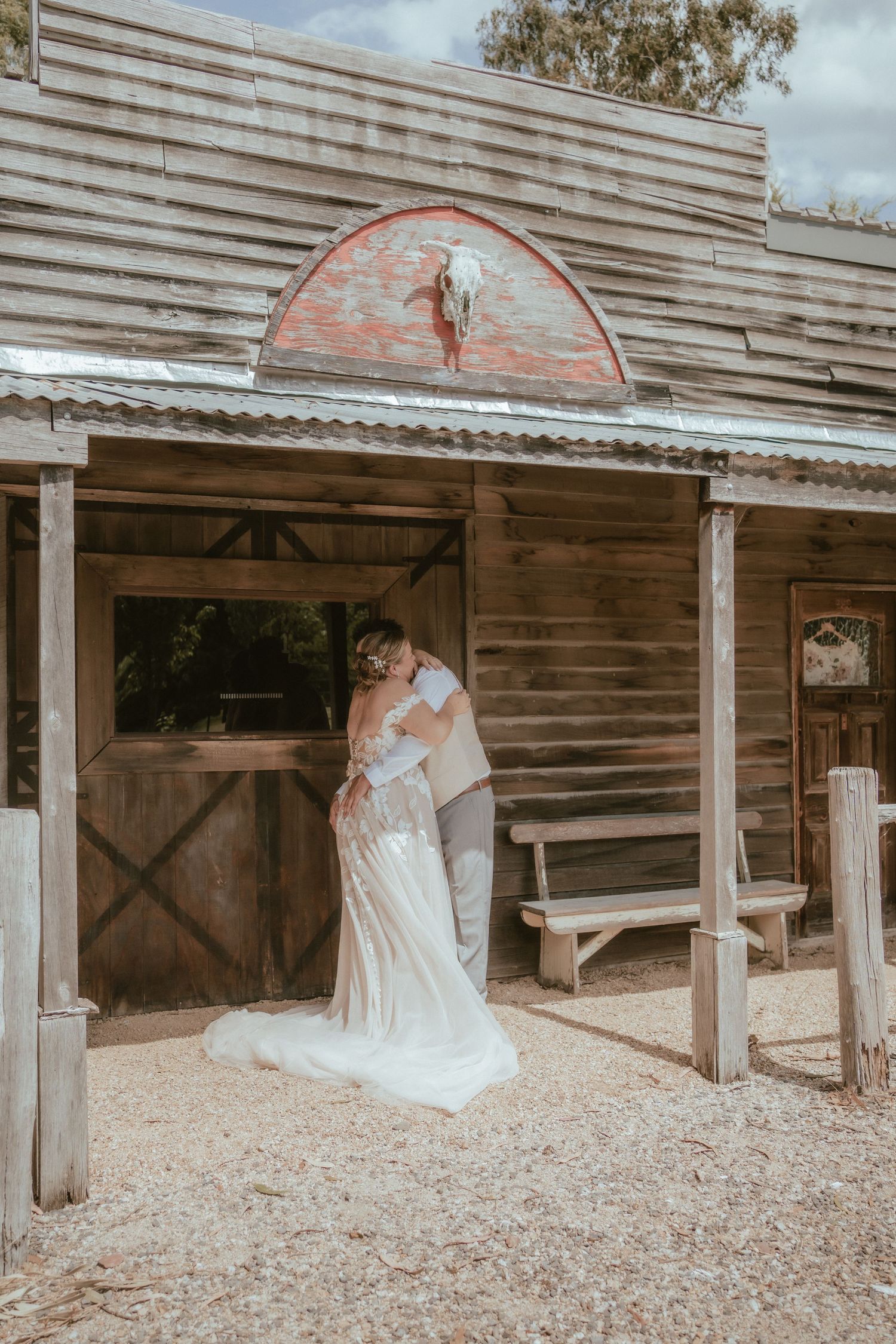 A vintage rustic barn wedding venue with wooden siding and covered outdoor areas captures a romantic moment at sunset.