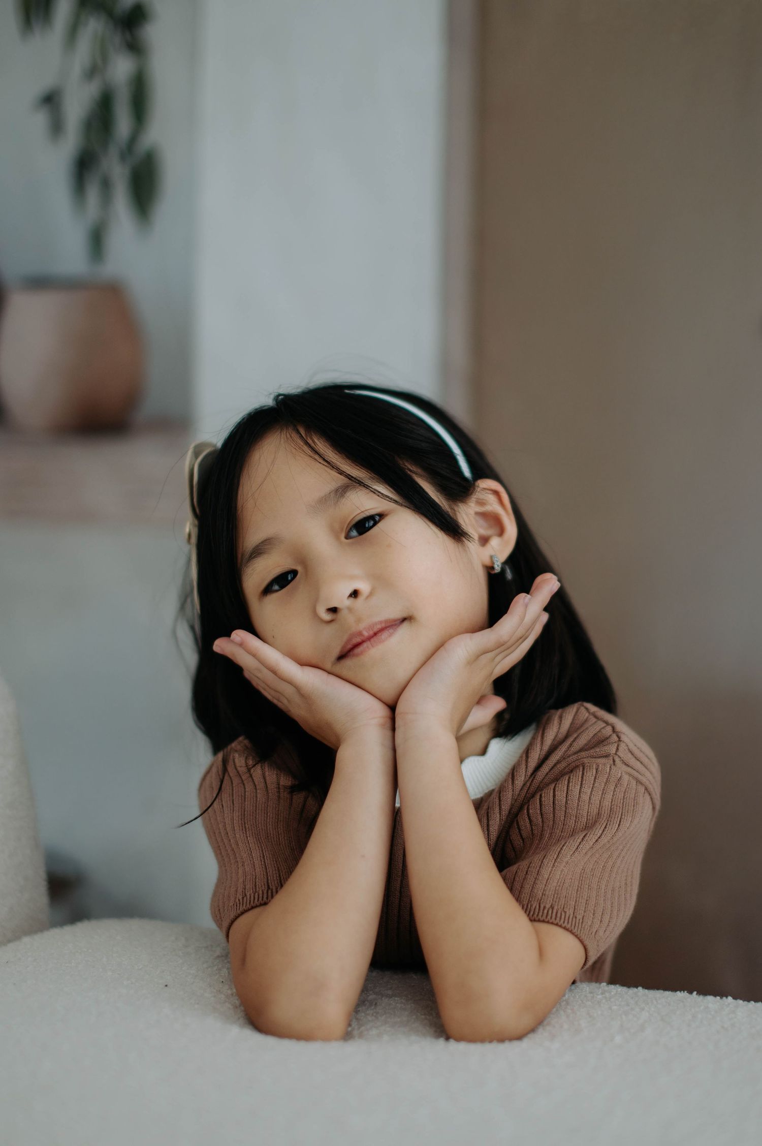Child lies on white bedding in warm moody lighting making playful expressions in a cozy indoor setting.