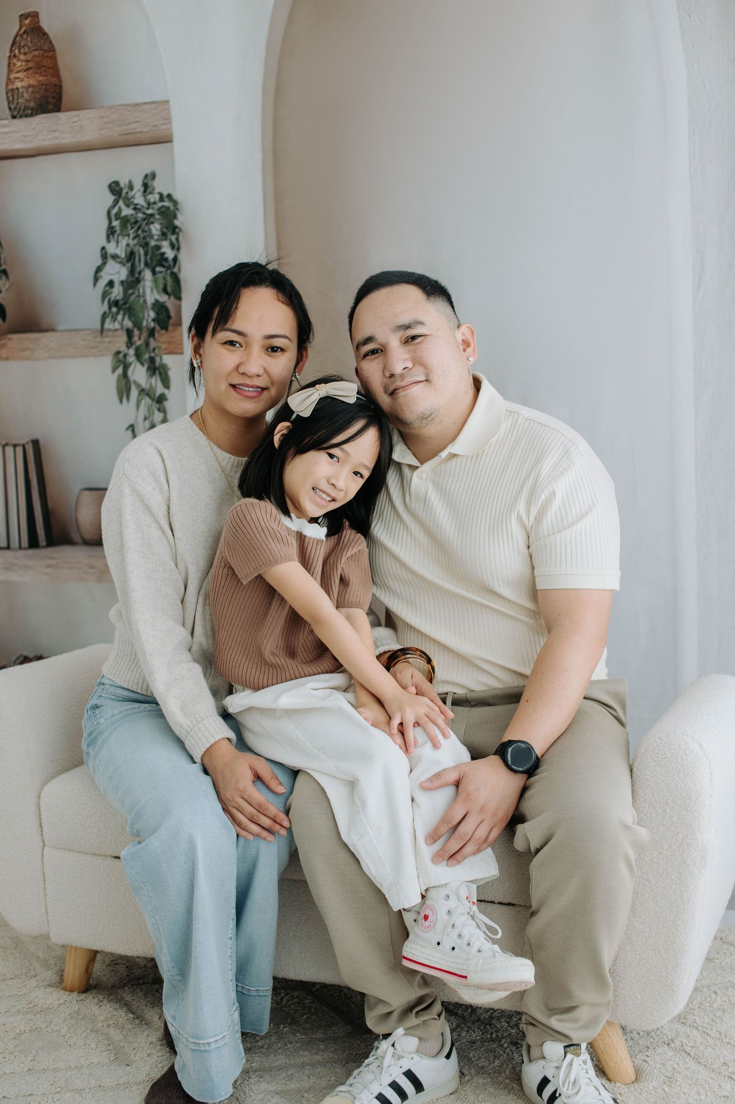 A couple wearing white sits together on a couch in a bright minimalist room with houseplants.