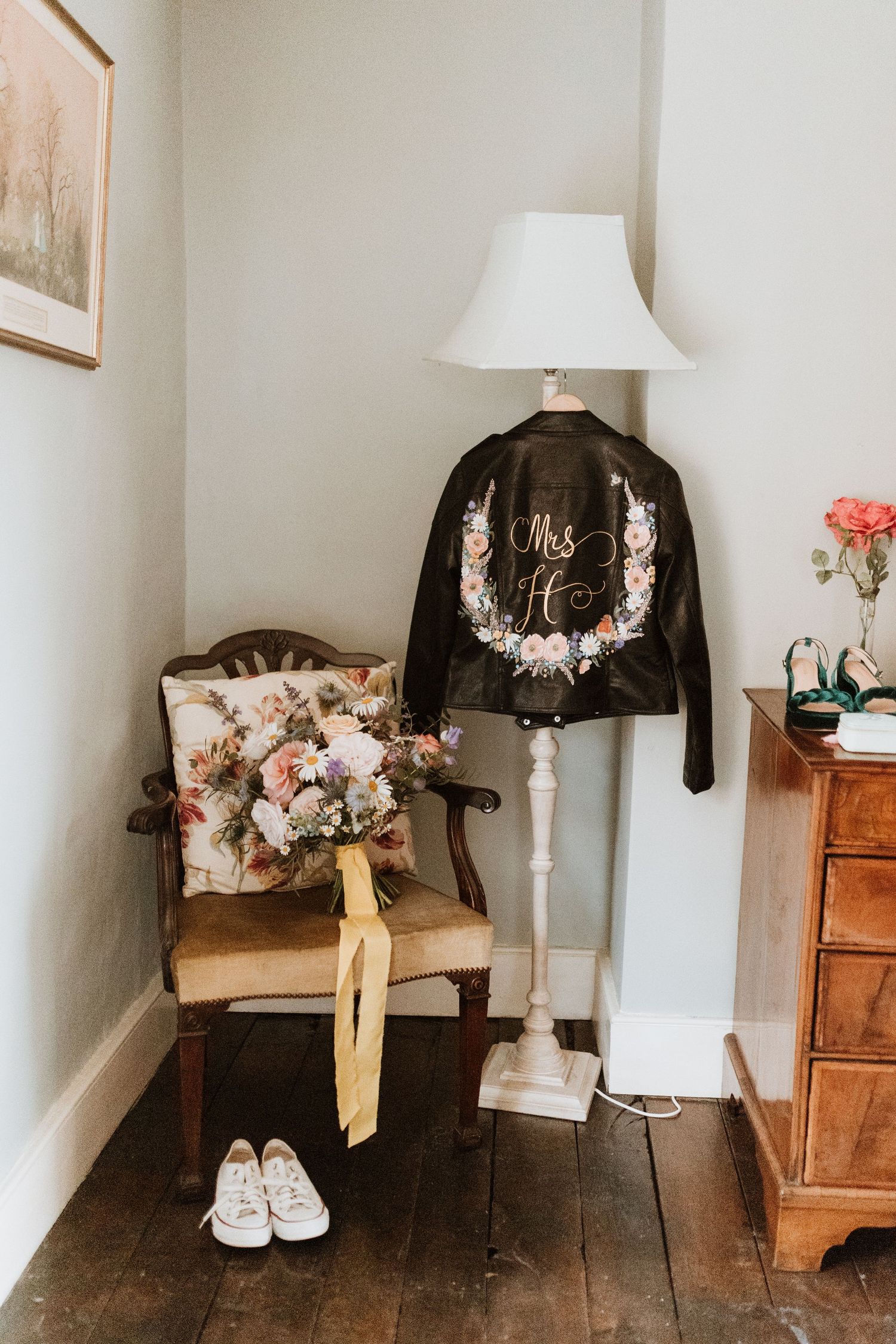 Custom leather jacket, floral bouquet, and white sneakers styled with vintage furniture in a cozy corner setting.