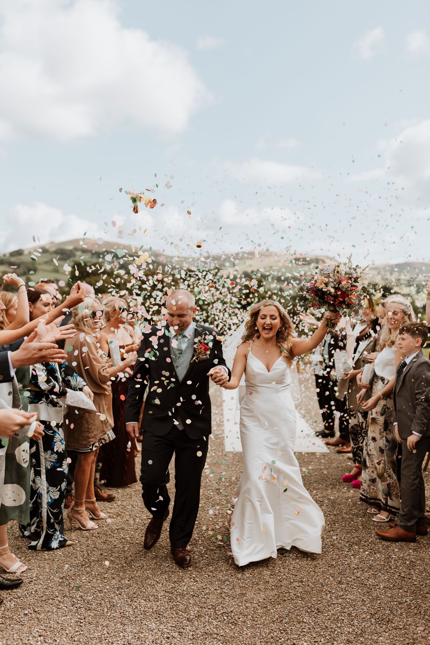 Wedding guests celebrate by tossing flower petals over the couple during an outdoor ceremony.