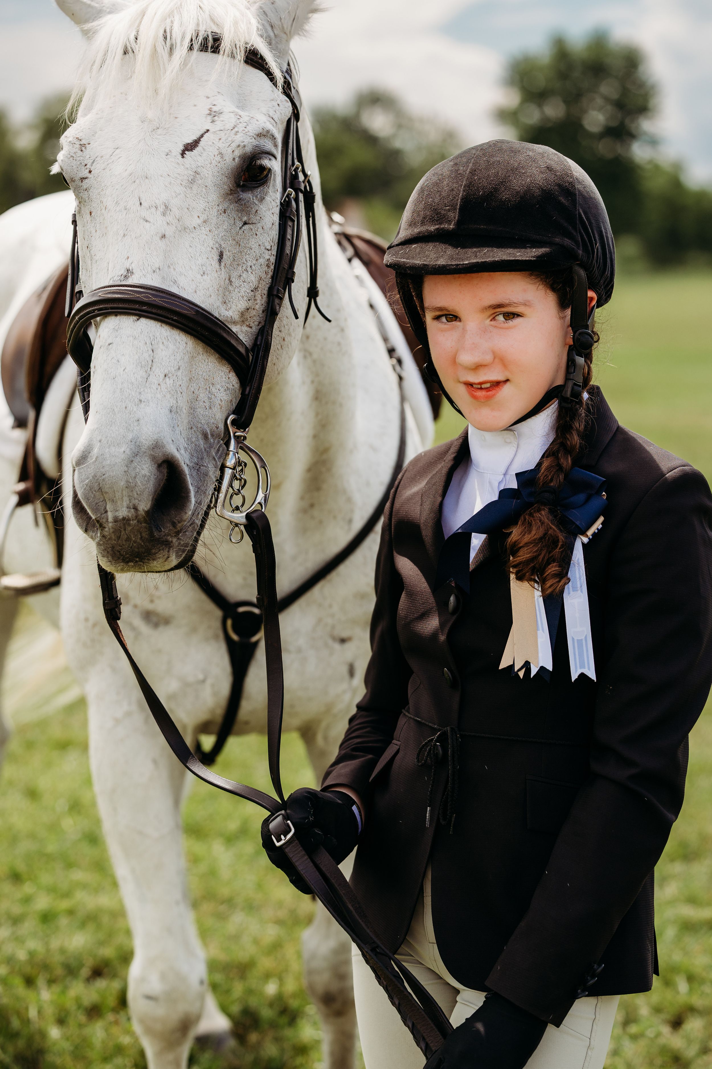 A beautiful white show horse with leather tack stands with its rider in formal equestrian attire.
