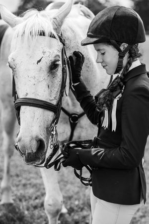 A tender moment between a white horse and rider in black show attire captured in black and white.