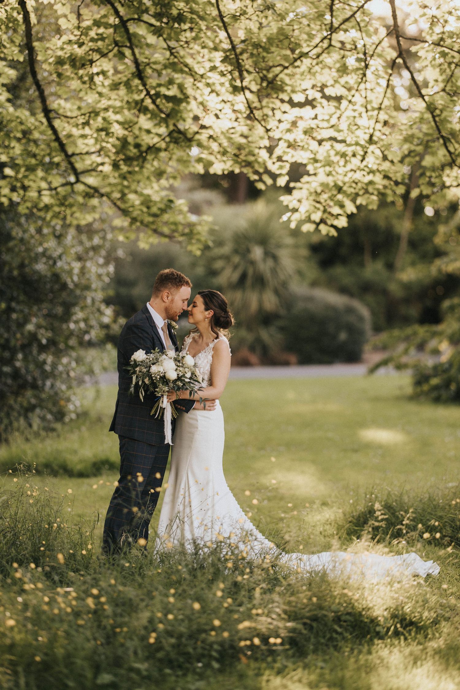A romantic wedding photo of a couple embracing under blooming spring trees in a sunlit garden setting - taken by Grimsby photographers.