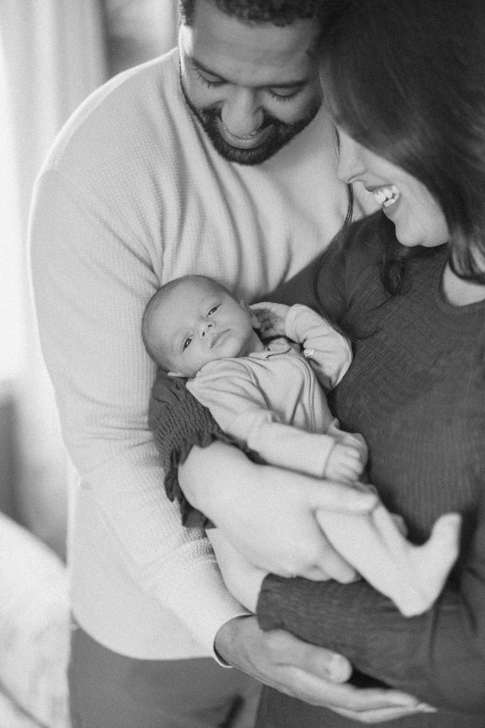 A tender black and white moment as parents cradle their newborn baby, sharing smiles and gentle embraces.