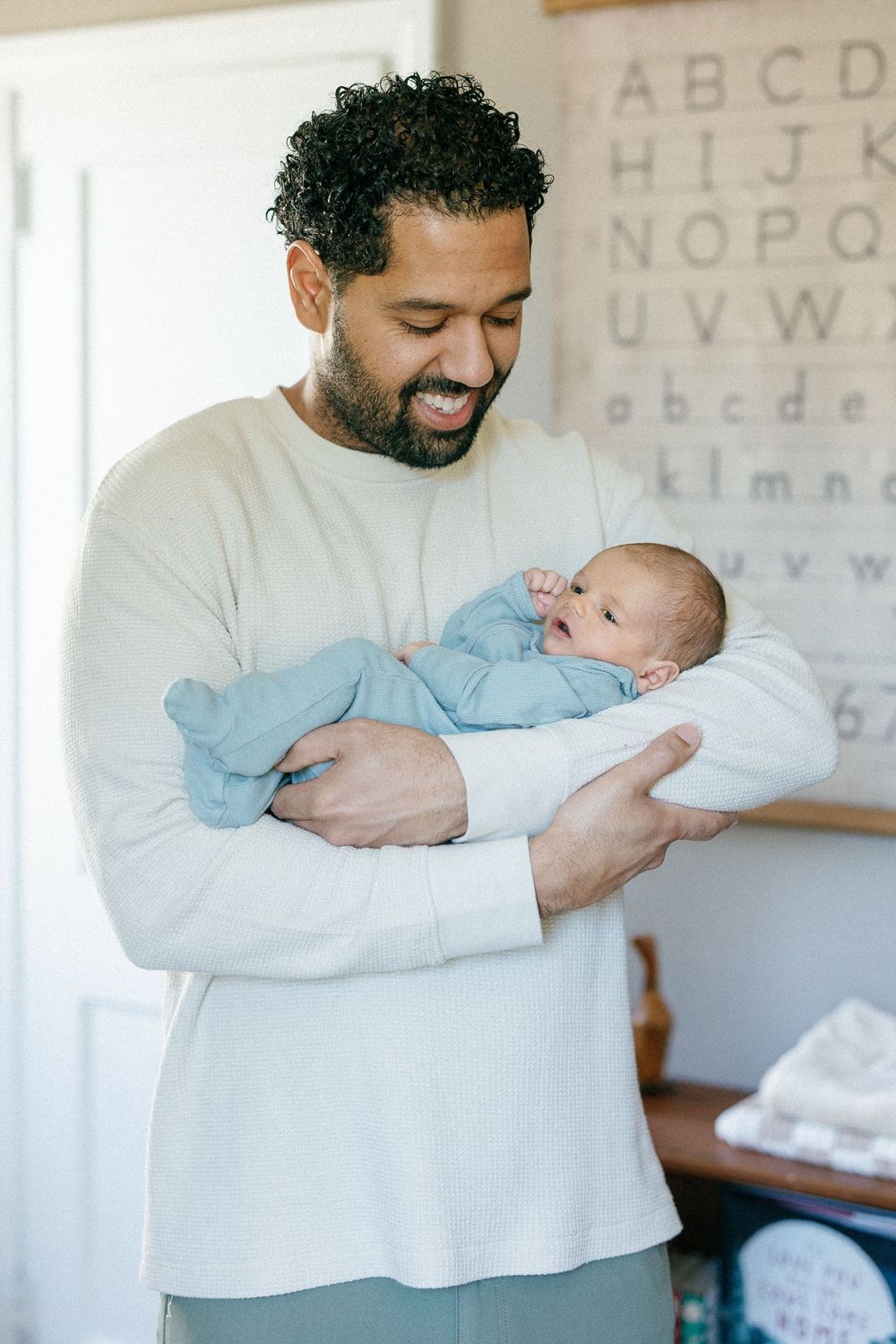 A loving parent wearing a cream sweater holds and gazes adoringly at a newborn baby in blue sleepwear.