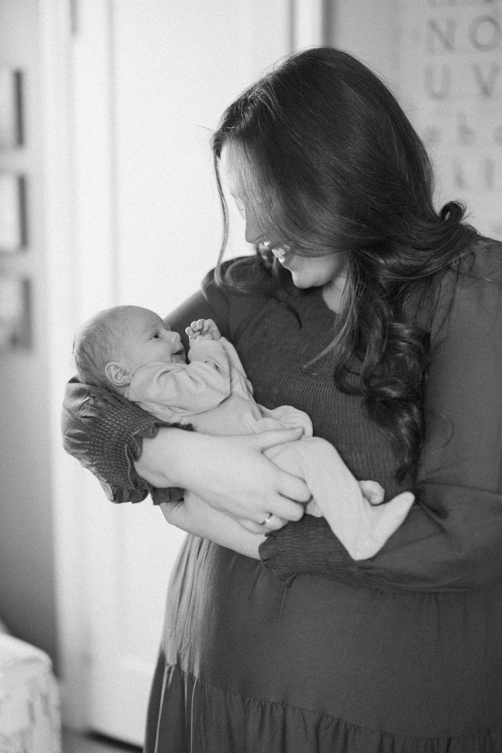 A tender black and white portrait of a woman in a long dress holding and gazing lovingly at her newborn baby.