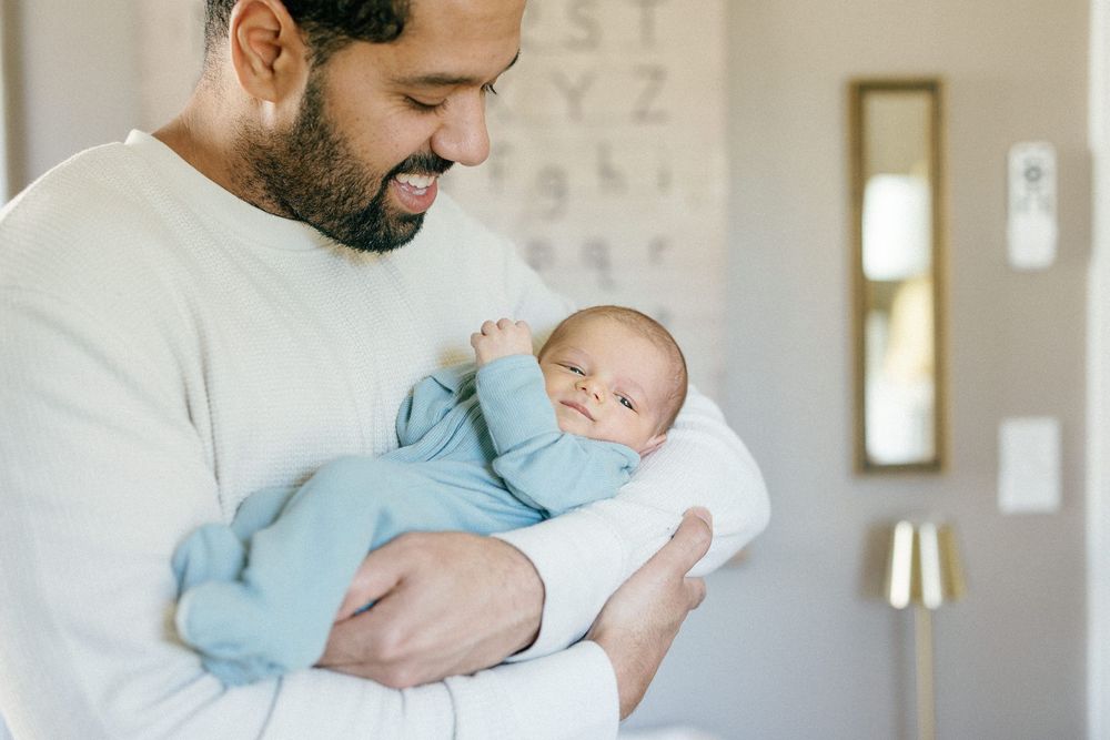 A parent in a white sweater tenderly holds a sleeping newborn baby wrapped in light blue and white blankets.