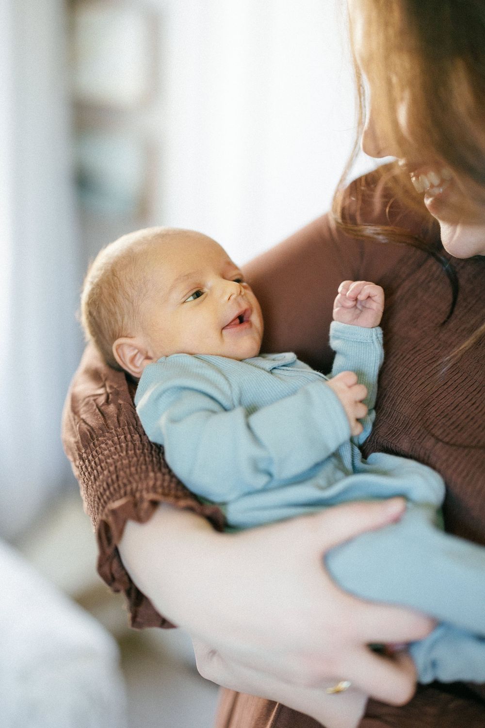 Sweet baby in light blue onesie smiles while being cradled in caregiver's arms.