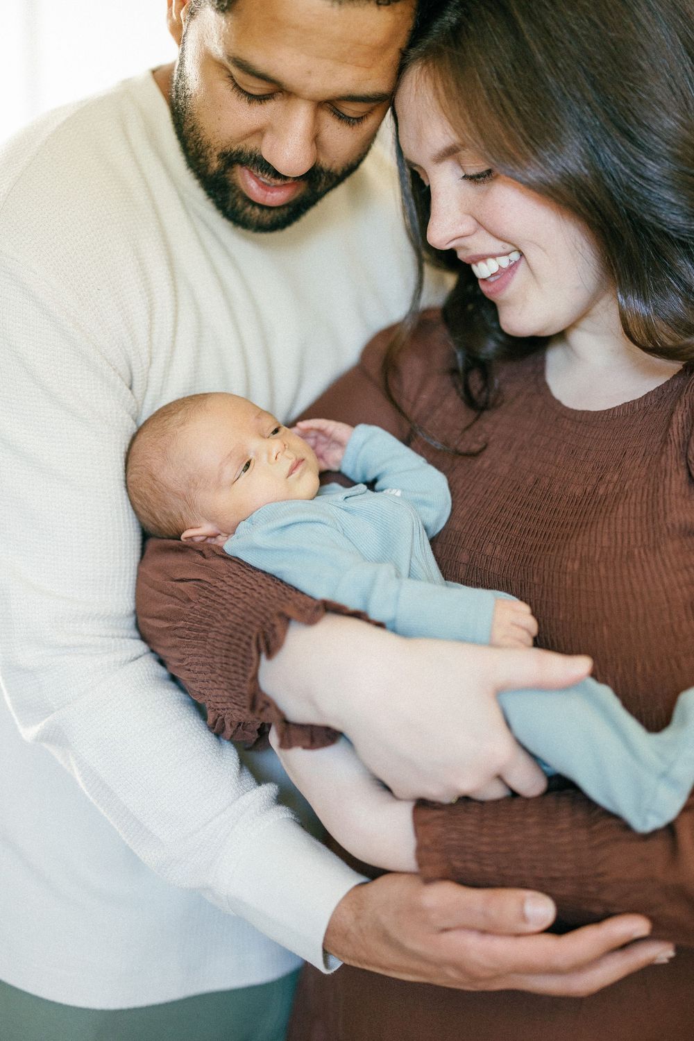 A couple lovingly holds their newborn baby in a series of tender moments captured against a light background.