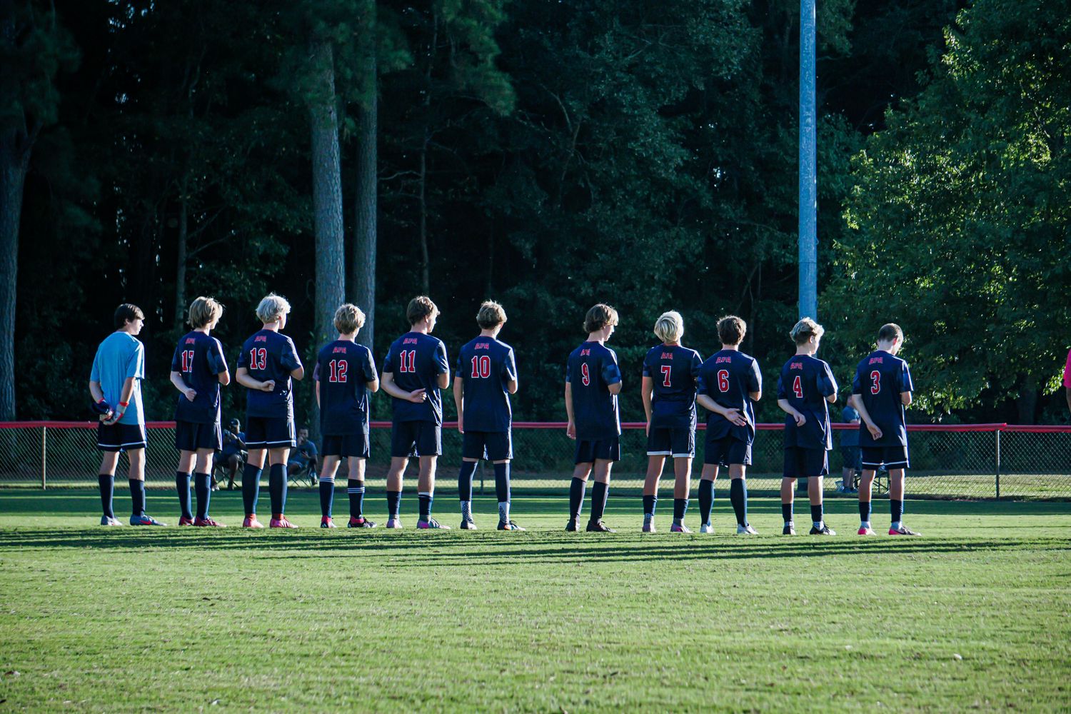 Patriots soccer team lines up on field before match in navy uniforms.